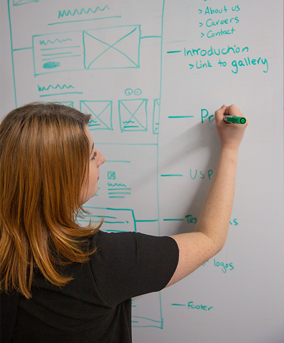 A designer drawing out a website wireframe on a whiteboard