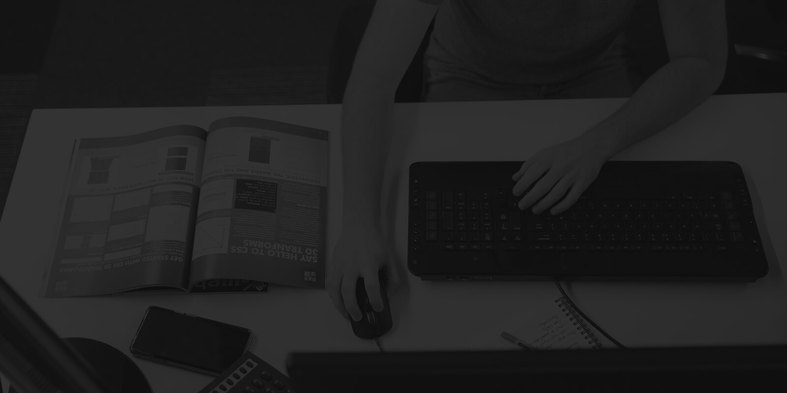 Person working on a computer at a desk with a magazine